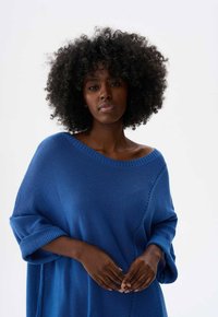 Blauwe gebreide oversized trui met een brede halslijn, opgerolde mouwen en een gestructureerde stof. Opvallend zijnaai-detail voegt extra interesse toe.