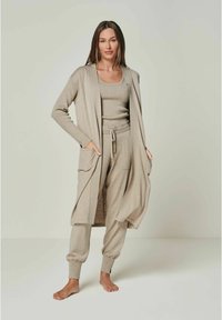 Beige Strick-Loungewear-Set, bestehend aus einem langen Cardigan mit Taschen, einem figurbetonten Oberteil und tapered Jogginghosen mit elastischen Bündchen. Glatte Textur.