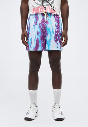 Męskie krótkie spodenki sportowe z fioletowo-niebieskim wzorem tie-dye, połączone z białymi wysokimi skarpetami i białymi butami sportowymi z czarnymi detalami.