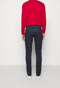 Mörkblå jeans med slim fit, med fickor med gula sömmar, kombinerat med en röd långärmad tröja och vita sneakers.