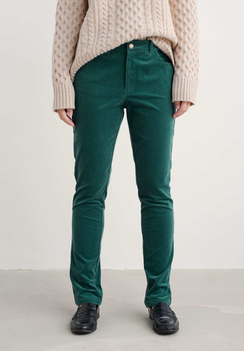 Zelené kordové kalhoty slim fit, se dvěma předními kapsami, zapínáním na knoflík a měkkým, texturovaným povrchem. Kombinované s krémovým pleteným svetr.