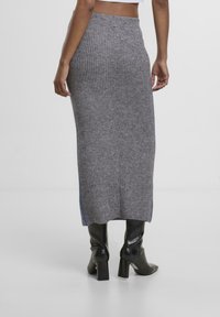 Grauer gerippter Strick-Maxi-Rock mit einem figurbetonten Bund, der seitliche Schlitze mit blauen Akzenten aufweist. Getragen mit schwarzen Absatzstiefeln.