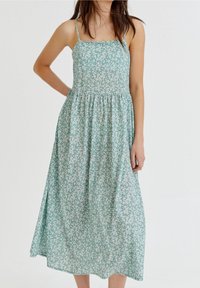 Vestido midi verde con flores, tirantes finos, escote cuadrado y cintura fruncida. La tela presenta un pequeño patrón de flores blancas.