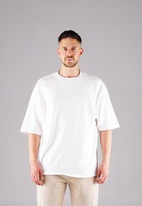 White oversized cotton t-shirt with a round neckline and short sleeves, featuring a subtle embossed logo on the chest.