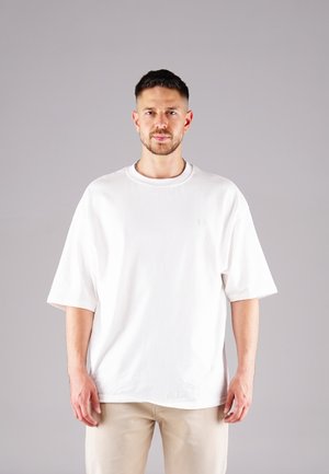 White oversized cotton t-shirt with a round neckline and short sleeves, featuring a subtle embossed logo on the chest.