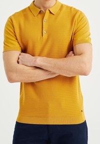 Yellow short-sleeve polo shirt with textured fabric, three-button placket, and ribbed collar, featuring subtle horizontal stripes and a logo detail.