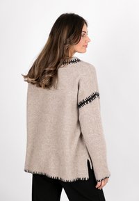 Beige Wollpullover mit lockerer Passform, der schwarze gestickte Akzente an den Schultern und am Saum sowie eine seitliche Schlitzdetails aufweist.