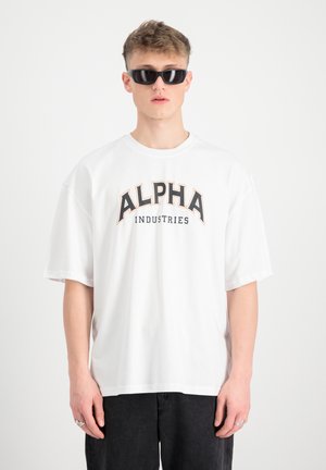 Weißes, übergroßes Baumwoll-T-Shirt mit dem "ALPHA INDUSTRIES"-Grafik in Schwarz und Orange. Das Modell trägt schwarze Sonnenbrillen. Einfaches Design, kurze Ärmel.