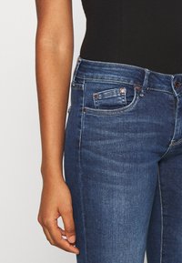 Mörkblå denimjeans med smal passform, med framfickor, kopparfärgad hårdvara och ett lätt slitage på tyget.