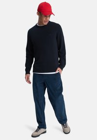 Marineblå strikkegenser med rund hals, kombinert med marineblå cordbukser. Modellen har på seg en rød cap og grå sko med svarte lisser.