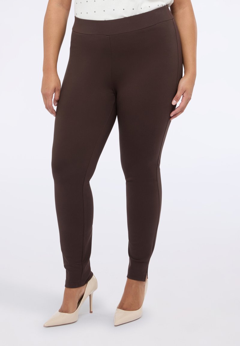 Leggings marrones elásticos con una textura suave y aberturas en los tobillos, combinados con tacones altos beige. La cintura es elástica y se sitúa en la cintura.