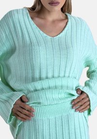 Lysegrøn strikket sweater med V-hals, ribstrik og løse ærmer. Stoffet virker blødt og let elastisk.
