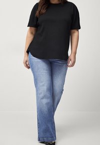 Top corto a maniche corte nero con texture abbinato a jeans a gamba dritta azzurri chiari. L'outfit presenta una vestibilità comoda e spaccature laterali all'orlo.