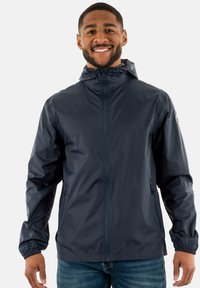 Veste à capuche navy en matériau léger et résistant à l'eau, avec des poignets élastiques, deux poches latérales et une fermeture éclair complète. Logo sur la manche.