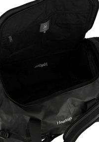 Schwarze Duffel-Tasche aus wasserdichtem Material mit Reißverschluss und einem Innenetikett. Das Innere ist geräumig und unauffällig.