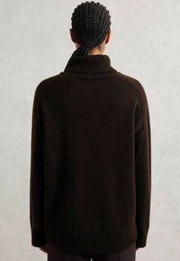 Suéter de punto marrón oscuro con un cuello alto, puños y dobladillo acanalados. El diseño presenta un corte holgado y costuras de hombros caídas.