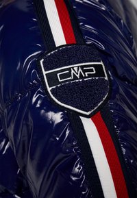 Giubbotto imbottito blu navy con texture lucida, accentato da strisce bianche e rosse, e un logo CMP ricamato a forma di scudo.