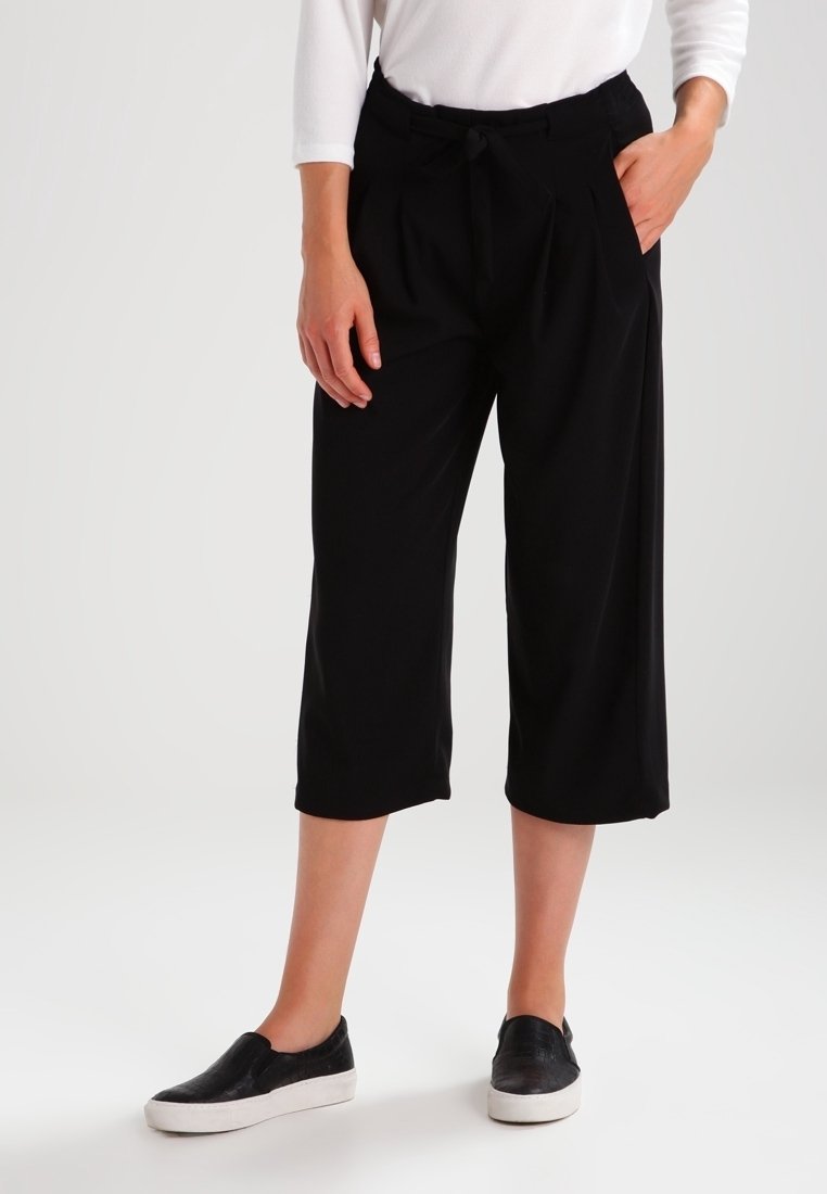 Pantalon court noir en tissu doux, avec taille à cordon de serrage et poches avant. Associé à des chaussures noires faciles à enfiler.