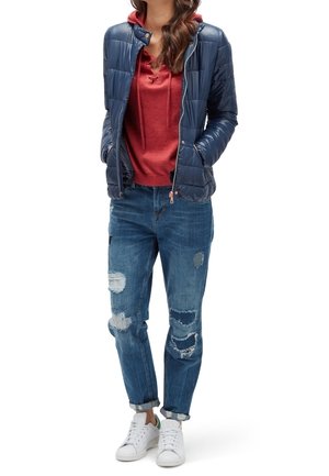 Navy quilted puffer jacket, red hoodie with drawstrings, distressed blue denim jeans, and white sneakers. Casual layered outfit.