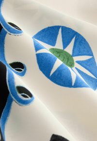 Biely textil s modrými a zelenými hviezdicovými kruhovými vzormi a čiernymi oválnymi tvarmi s modrými obrysmi, zobrazený s viditeľnými záhybmi a textúrou.