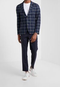 Marineblå rutigt blazer i texturerad tyg, med en enkel knäppning. Kombineras med marinblå byxor och vita sneakers.