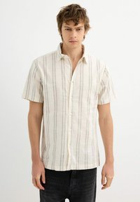 Camisa de manga corta en tejido crema claro con rayas verticales negras, con un cierre de botones en la parte delantera y un ajuste relajado.