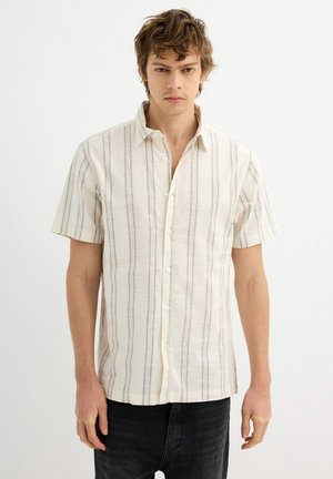 Camisa de manga corta en tejido crema claro con rayas verticales negras, con un cierre de botones en la parte delantera y un ajuste relajado.