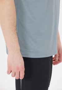 Harmaa nopeasti kuivuva urheilupaita, jossa on sileä rakenne, lyhyet hihat ja helman etiketti. Yhdistetty mustiin tiukkoihin leggings-housuihin, joissa on kuvio.