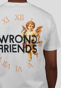 Bílý bavlněný tričko s motivem cheruba a květinovými prvky, překryté nápisem "WRONG FRIENDS" výrazným černým písmem, obklopené oranžovými římskými číslicemi.