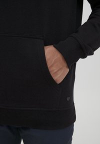 Felpa nera con tasca frontale, polsini e orlo a costine. Tessuto morbido e dettagli del logo discreti sul lato inferiore.