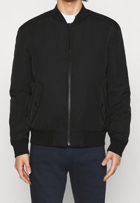 Giacca bomber nera con zip frontale, tasche laterali, polsini e orlo a costine. Realizzata in tessuto liscio con un design semplice e classico.