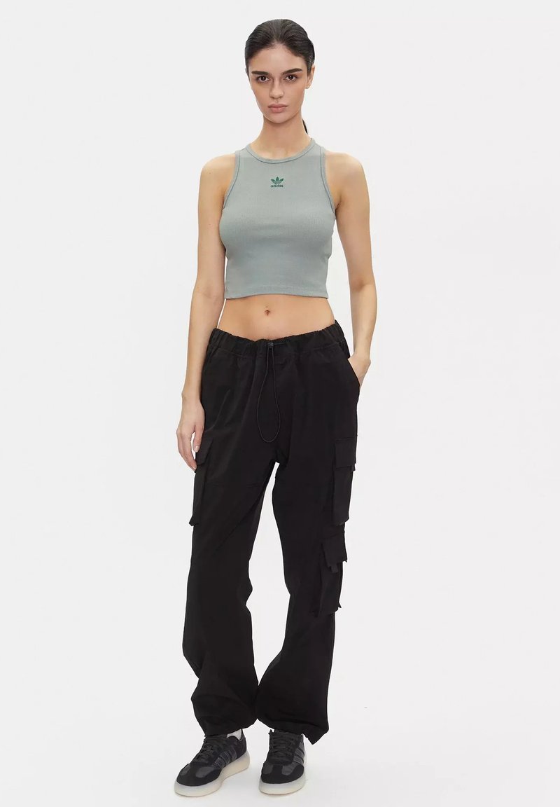 Top corto grigio a costine con logo verde, abbinato a pantaloni cargo neri con molte tasche e vita con cordino. Sneakers nere.