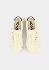 Baskets couleur crème avec une finition en cuir lisse, bout rond et accents noirs au talon. Logo "BOSS" imprimé sur la languette.