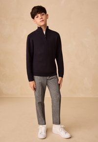 Tumehämaras sinises poollukuga kraega puuvillasest segust pullover, kombineeritud halli ruudulise püksiga ja valgete tossudega. Lihtne disain, lõdvestunud lõige.