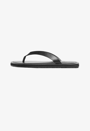 Chancla plana negra de goma con una simple tira en forma de T y suela texturizada, mostrada de lado sobre un fondo blanco.