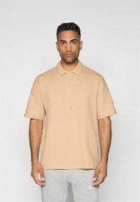 Beige polo shirt met een gestructureerd patroon, korte mouwen en een halve rits kraag. Bevat een klein geborduurd logo in het midden.