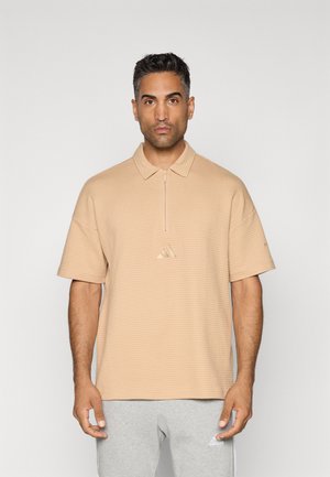 Beige polo skjorte med teksturert mønster, kortermer og halv-glidelås krage. Har en liten brodert logo i sentrum.