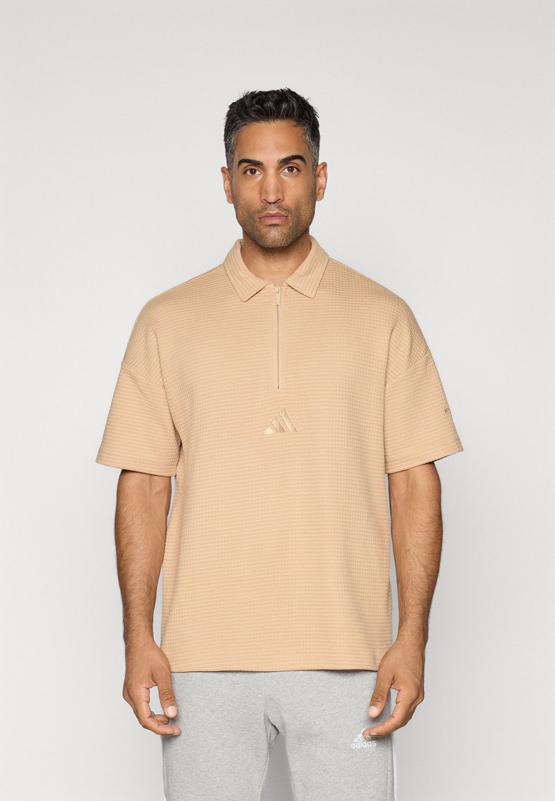 Beige polo shirt met een gestructureerd patroon, korte mouwen en een halve rits kraag. Bevat een klein geborduurd logo in het midden.