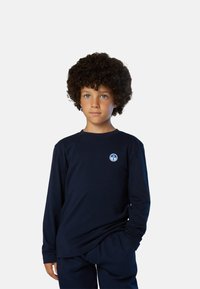 Camisa de manga larga azul marino de algodón, con un pequeño logotipo azul circular en el pecho. Combinada con pantalones azul marino a juego.