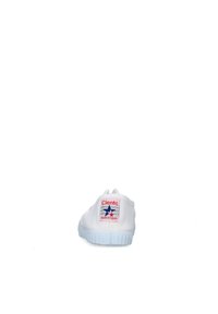 Baskets en toile blanches avec une surface texturée, arborant une étiquette de logo rouge et bleu, un bout rond et une semelle en caoutchouc avec des rainures horizontales.