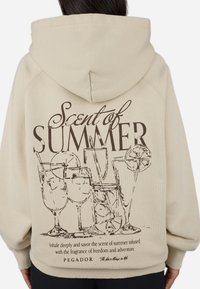 Beige hooded sweatshirt featuring a print of cocktail glasses and the text "Scent of Summer" in dark brown. Soft fabric, relaxed fit.