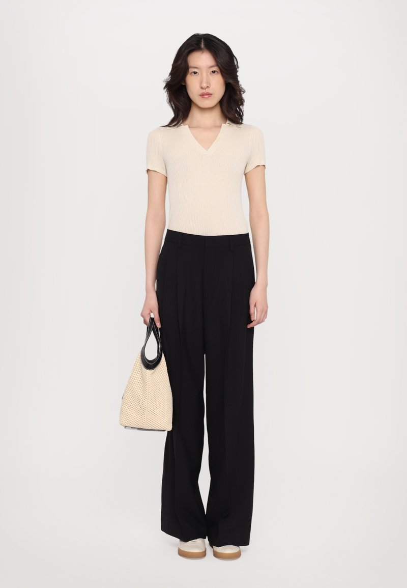 Beige ribbed short-sleeve top, black wide-leg trousers, holding a textured beige bag with black accents, paired with cream shoes.