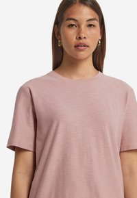 Rosenfärgad t-shirt med rund halsringning, korta ärmar och ett mjukt, något texturerat tyg. Enkelt design utan mönster eller ytterligare detaljer.