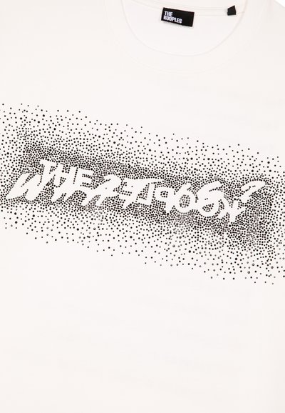 Camiseta branca com um design gráfico preto. O texto aparece num estilo distorcido, acentuado por um padrão de pontos que transita em densidade.