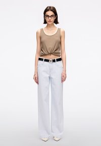 Jeans de pierna ancha azul claro, top de canalé beige con un nudo en el frente y un cinturón negro con herrajes plateados. Zapatos blancos de punta.