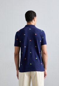 Námořnická polokošile s barevnými vyšívanými vlajkami rozptýlenými po zádech. Má klasický límec a krátké rukávy, je vyrobena z měkkého bavlněného materiálu.