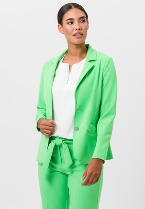 Felgroene blazer van gladde stof, met een enkele knoopsluiting en twee voorzakken, gecombineerd met bijpassende broek en een witte top.