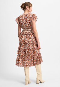 Blumen-Maxikleid mit Rüschenschultern und gestuftem Design in Orange- und Blautönen. Beinhaltet einen hellbraunen Gürtel. Paar cremefarbene Knöchelstiefel.
