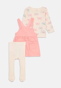 Rosa Corduroykleid mit Taschen und Knopfträgern, beiges Langarmshirt mit Schleifenmuster und weiße Leggings.