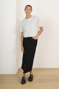T-shirt gris clair à manches courtes avec des embellissements subtils, associé à une jupe maxi en denim noir avec une fente à l'avant. Mocassins noirs avec des accents dorés.
